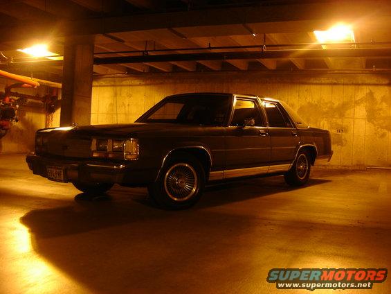 Dark sedan parked in a dimly lit garage, showing its front quarter view with chrome trim and wire wheels