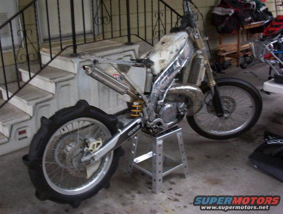 Dirt bike disassembled on a stand, showing engine and rear sand tire