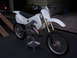 1999 Honda CR250R - A white dirt bike is positioned on a metal stand with wooden ramps in the background.