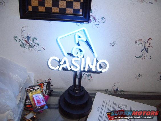 Casino neon sign with blue and white lights, on a black base, with a framed checkerboard above