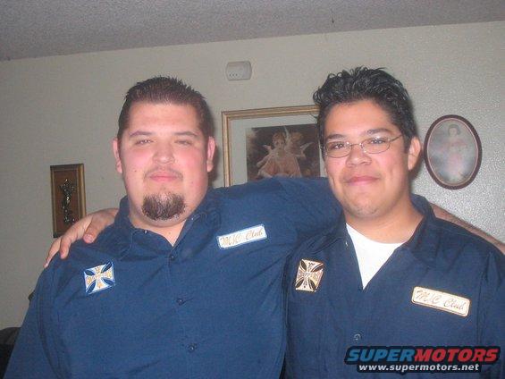 Two guys in matching blue shirts with patches that say "M.C. Club" and a cross emblem