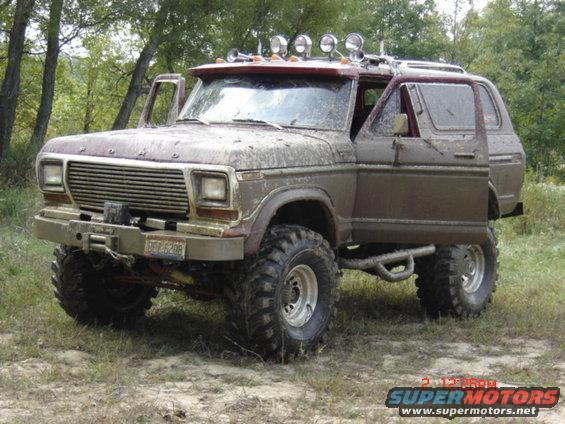 Muddy 1978 Ford Bronco with off-road tires, winch, and extra lights on roof. Doors are open