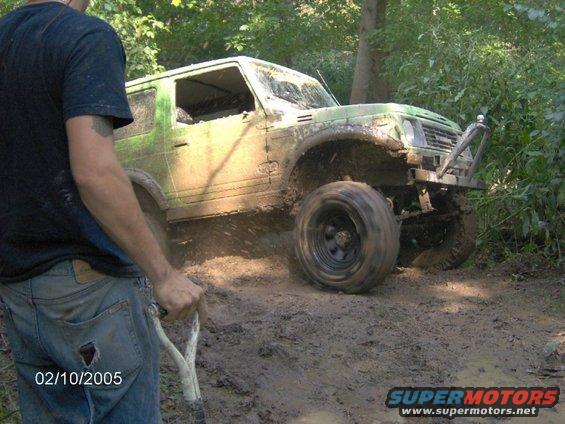 Mud-covered green off-road vehicle with a roll cage and aftermarket bumper, stuck in mud
