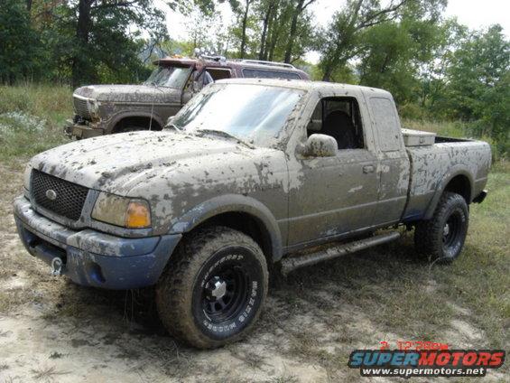 Mud-covered pickup truck, 3q-front view. Another vehicle is behind it