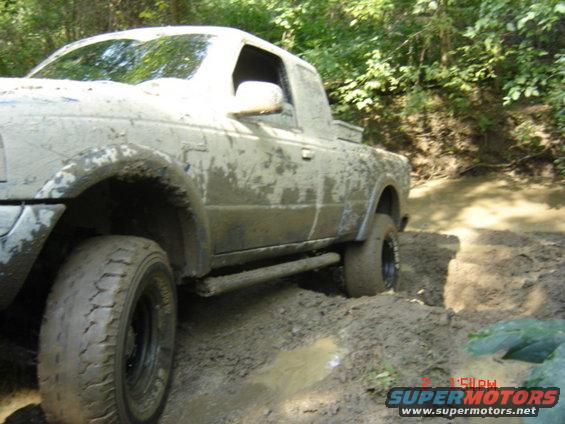 Mud-covered pickup truck navigating a muddy trail with trees in the background