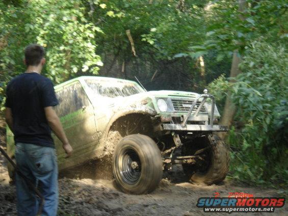 Green Suzuki Samurai stuck in mud on a wooded trail, person watching