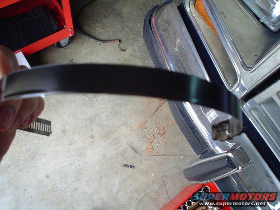 Hand holding black trim piece near 1984 Ford Bronco fender and grille