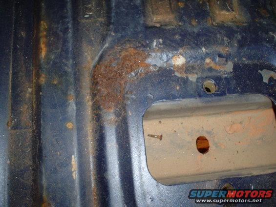 Rusted blue interior floor pan with a screw in a metal bracket