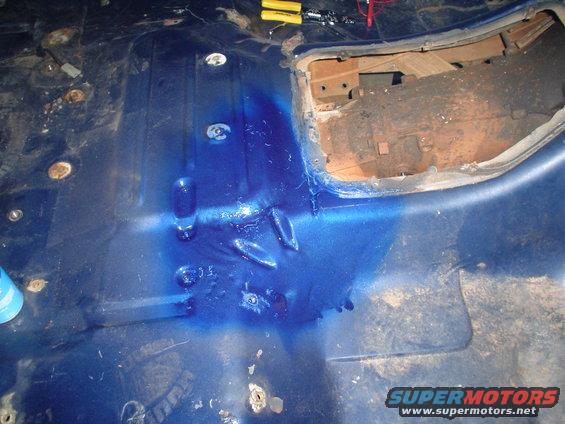 Blue painted vehicle floor with rust spots and a cut-out section revealing mechanical components