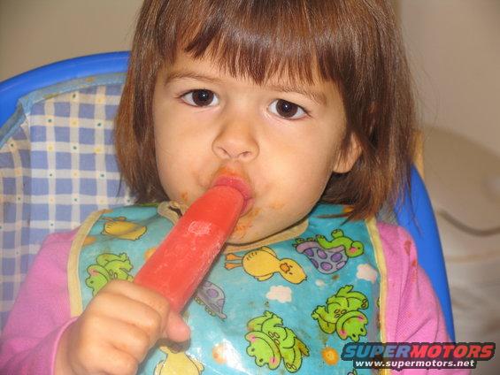 Child in a high chair wearing a bib and eating a red popsicle