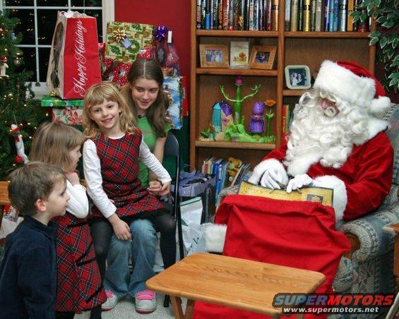 Santa reading to children near Christmas tree and gifts