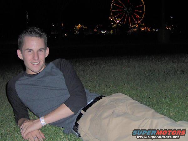 Man lying on grass at night, Ferris wheel illuminated in the background