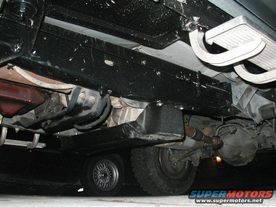 Underside view of a vehicle's frame, suspension, and drivetrain components. A spare tire is visible below