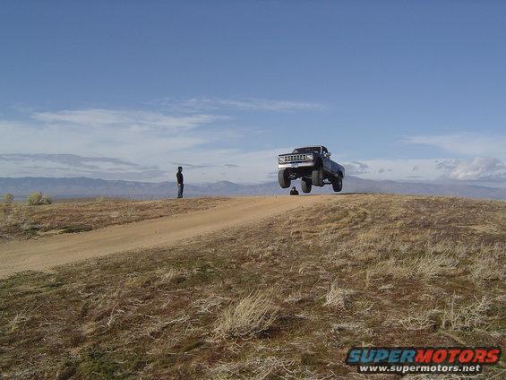 Truck airborne over a dirt hill, person watching