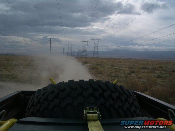 Spare tire in truck bed, driving on dusty road with power lines overhead