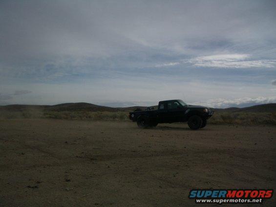 Black pickup truck driving on a dirt road with hills in the background