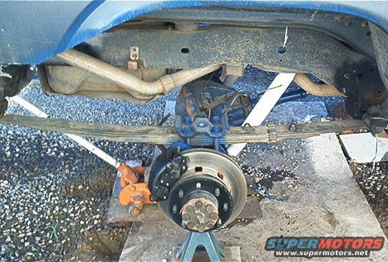 Rear axle assembly with leaf springs, shock absorber, and brake rotor. Vehicle is supported by jack stands