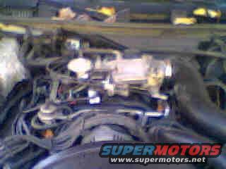 Engine bay with hoses, wires, and a throttle body. Supermotors.net logo at bottom