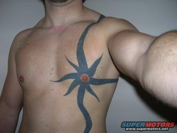 Man's torso with a large blue tribal tattoo and a red-centered circular design. Watermark reads SUPERMOTORS