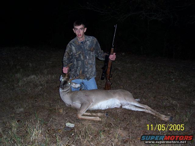 guy holding a deer he shot, rifle nearby