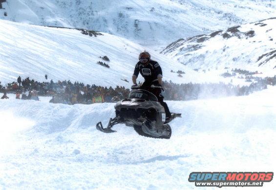 Snowmobile airborne with rider, front view. Crowd watches in background