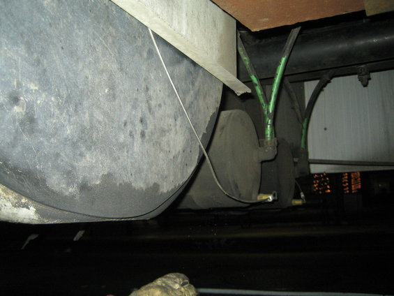 Undercarriage of a vehicle showing two large grey tanks, green hoses, and black pipes