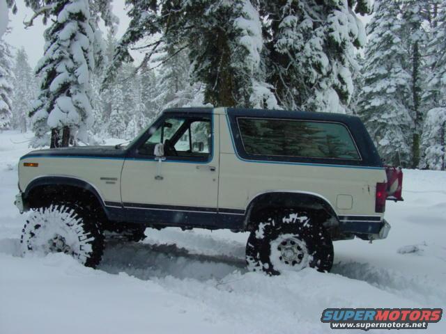 1986 Ford Bronco driving through deep snow, side view