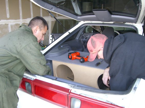 1996 Ford Probe trunk with custom subwoofer box and two men working on it. Orange drill visible