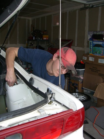 Man working on car trunk, red taillight visible