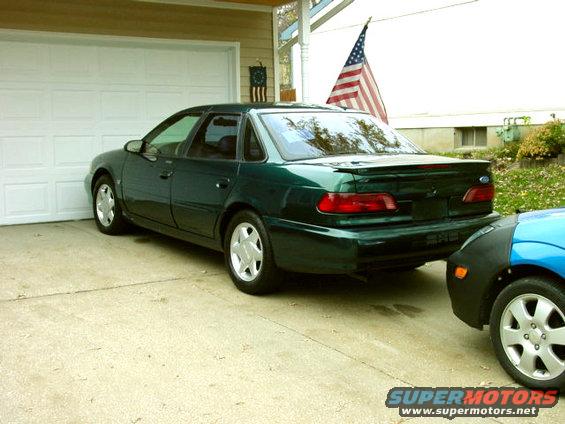 green sedan parked next to a blue car in a driveway, american flag visible