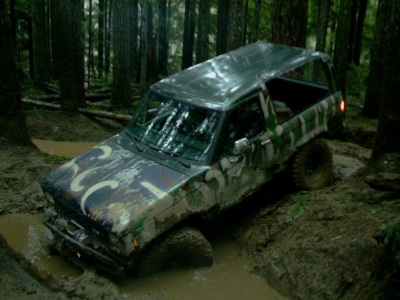 1987 Ford Bronco II with camouflage paint stuck in mud, trees in background