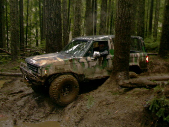 Camouflaged SUV driving through mud in a forest