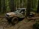 1987 Ford Bronco II - This vehicle is navigating a muddy trail surrounded by dense trees.