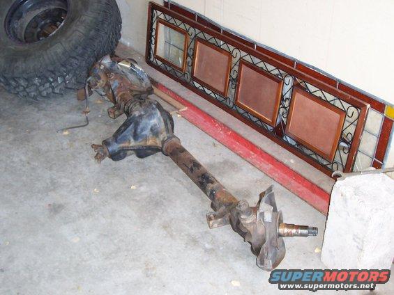Front axle assembly with a large tire and a decorative mirror frame in the background