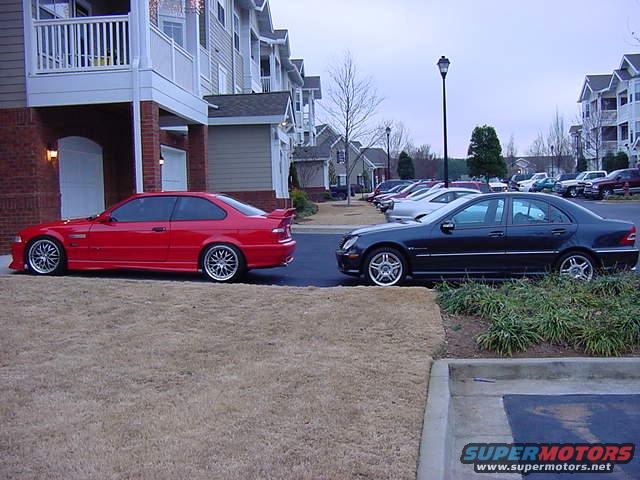 Dark sedan and red coupe parked on grass and asphalt