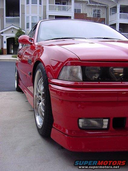 Red BMW coupe parked in front of apartment buildings. Front quarter panel and headlight visible