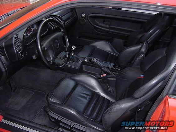 Interior view of a red 1995 BMW M3 showing black leather seats, dashboard, and gear shifter