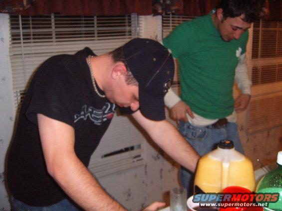 Two men indoors, one wearing a black t-shirt and baseball cap, the other a green t-shirt