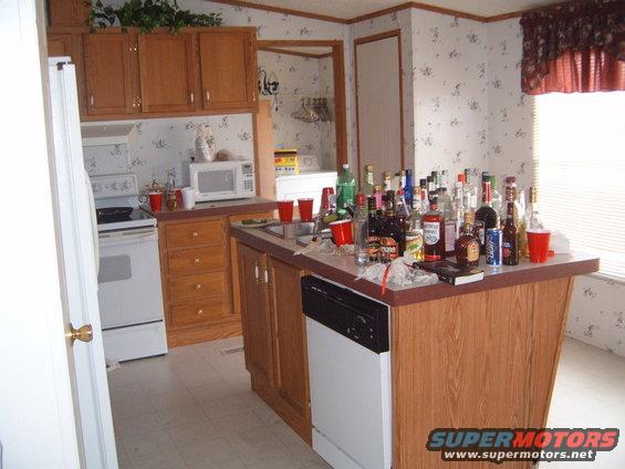 Kitchen counter cluttered with numerous alcohol bottles and red cups