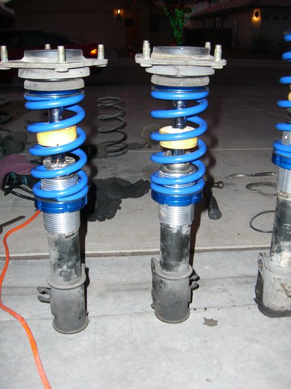 Three car suspension struts with blue springs and yellow cushions on a concrete surface