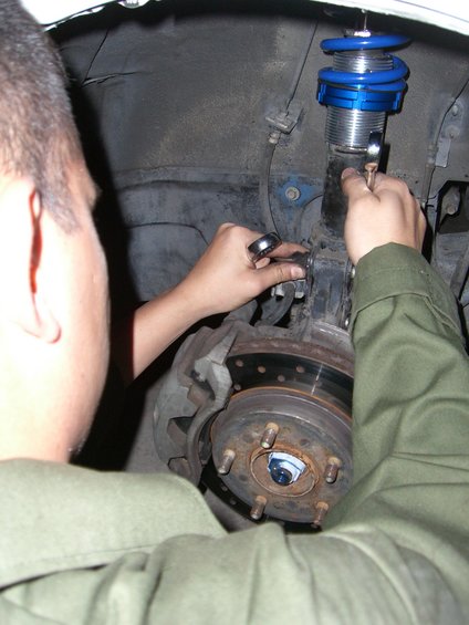 Car suspension assembly with blue adjustable coilover shock absorber and brake rotor being worked on by a person