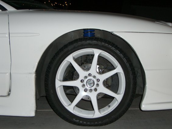 White car wheel with multi-spoke rims and blue coilover suspension visible behind fender