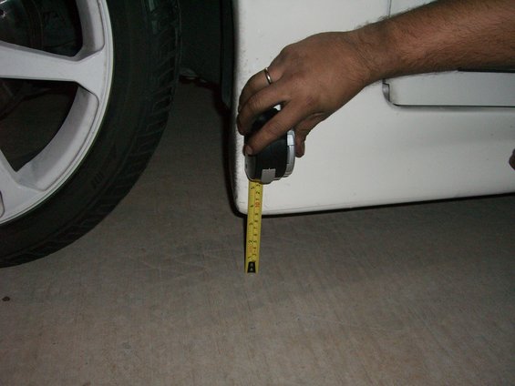 Measuring ground clearance on a white car's side skirt with a tape measure