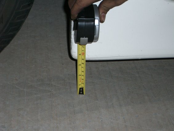 Hand holding tape measure to white car body near tire