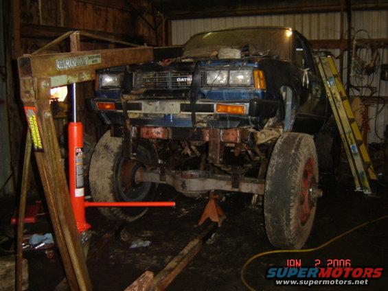 Front view of a blue pickup truck with DATSUN badging, on an engine hoist