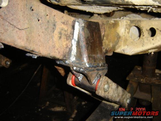 Close-up of a welded repair on a rusty vehicle frame with red bushings visible