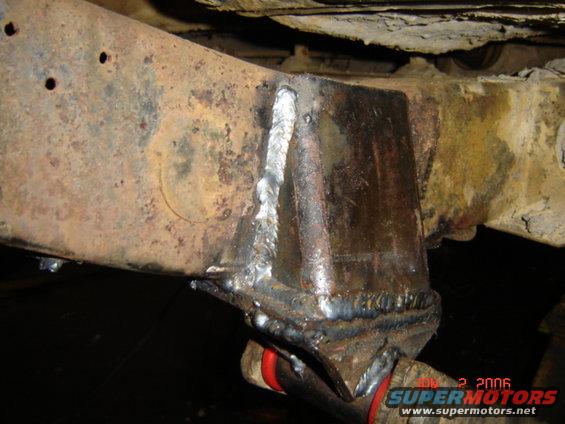 Rusty truck frame with a newly welded reinforcement bracket. Red bushings visible
