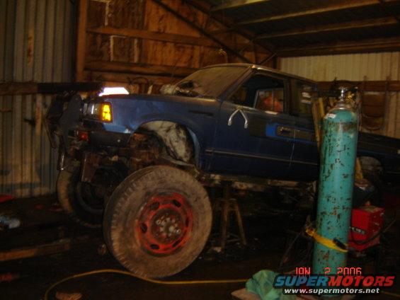 blue pickup truck on stands in a garage, looks like it's being worked on