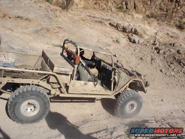 Off-road buggy with a bed and roll cage driving on a dirt hill