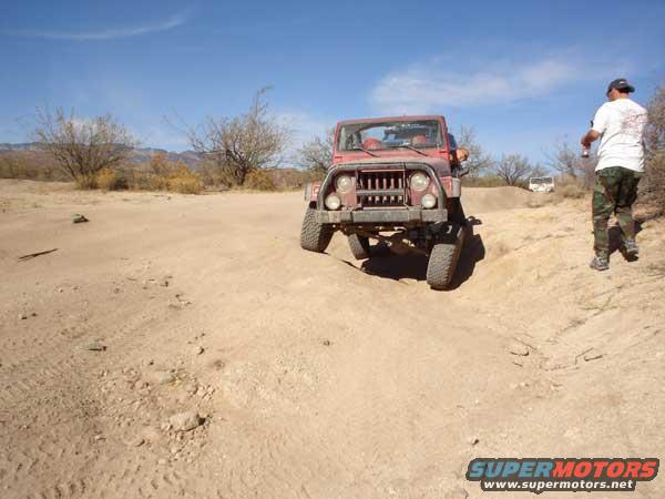 Red jeep on a dirt hill with a person standing nearby